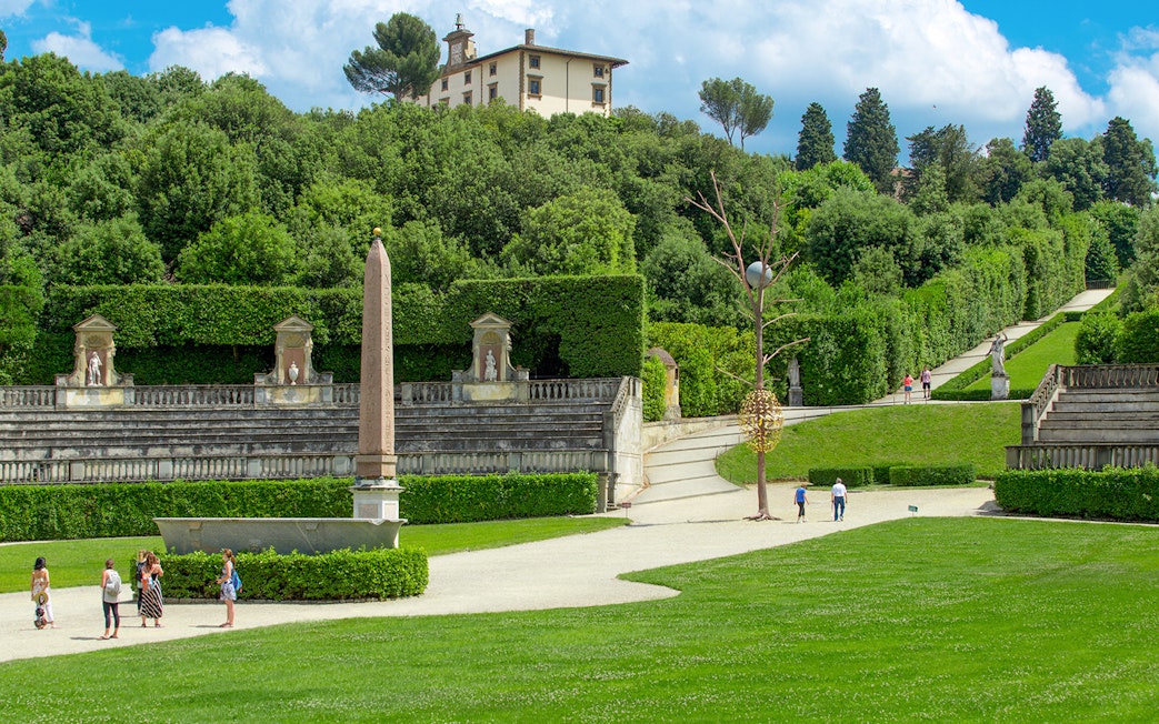 Visitors exploring Boboli Gardens with statues and obelisk, Florence.