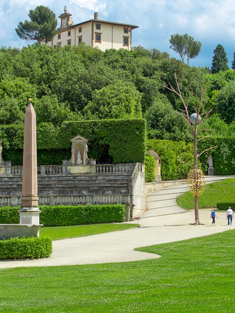 Visitors exploring Boboli Gardens with statues and obelisk, Florence.