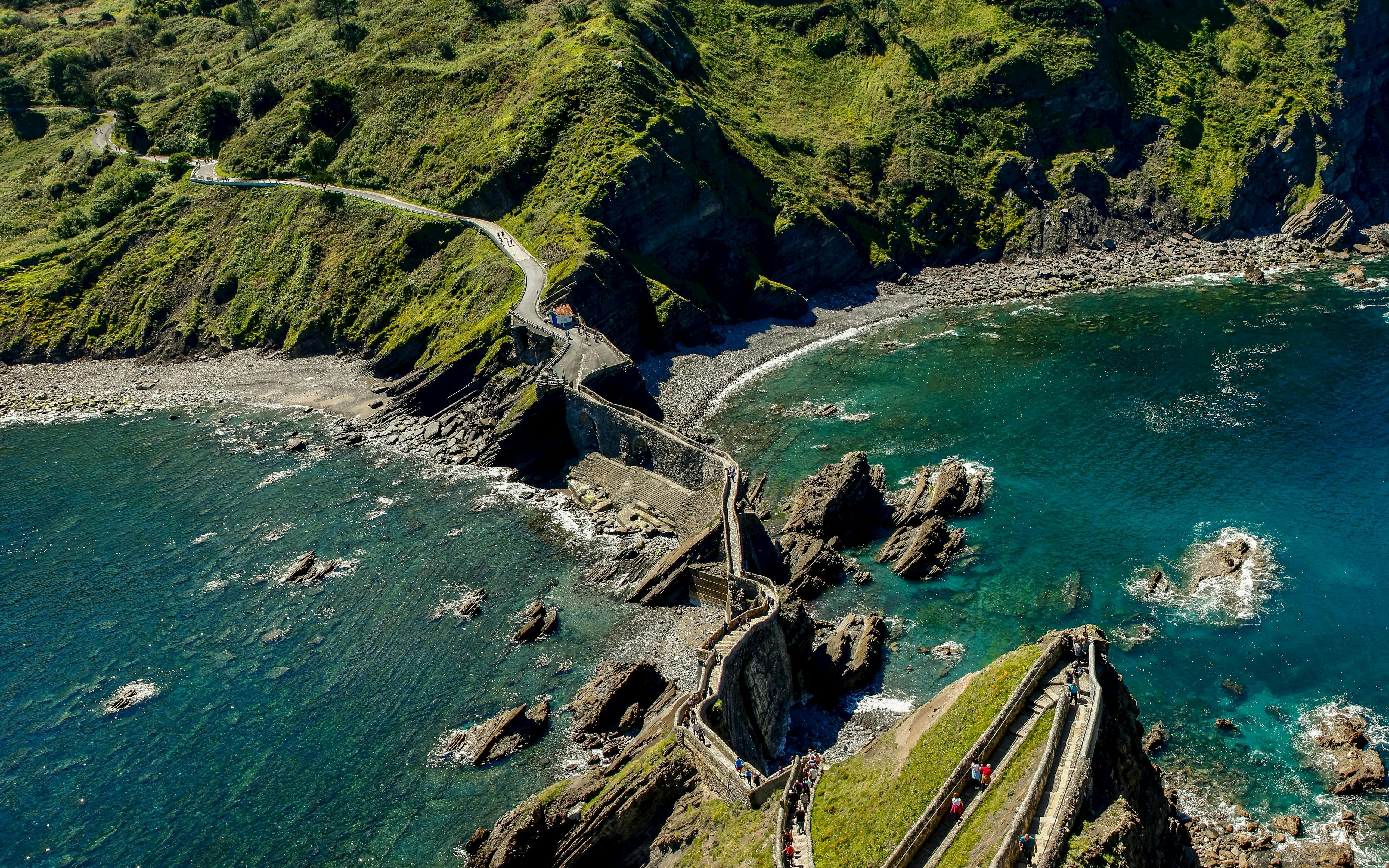 Pathway leading to Sant Juan de Gaztelugatxe hermitage surrounded by rocky coastline and blue sea.