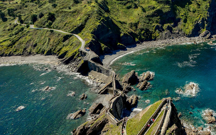 Pathway leading to Sant Juan de Gaztelugatxe hermitage surrounded by rocky coastline and blue sea.