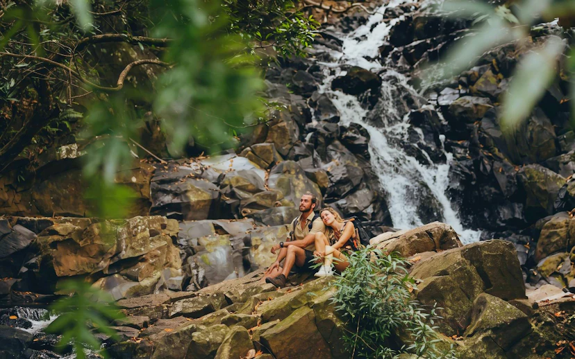 Couple sitting by a waterfall in Bel Ombre wilderness tour.