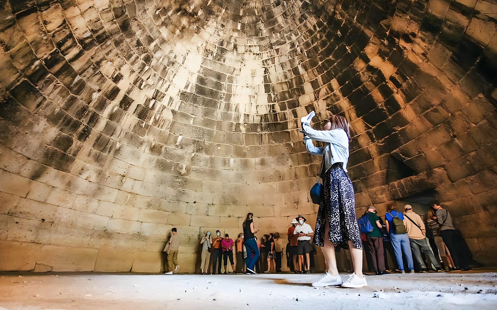 Tourists exploring the interior of the round tomb of Agamemnon in Mycenae.