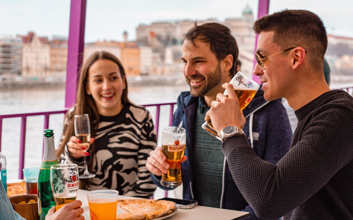 Group enjoying drinks and pizza on a Budapest party boat cruise.