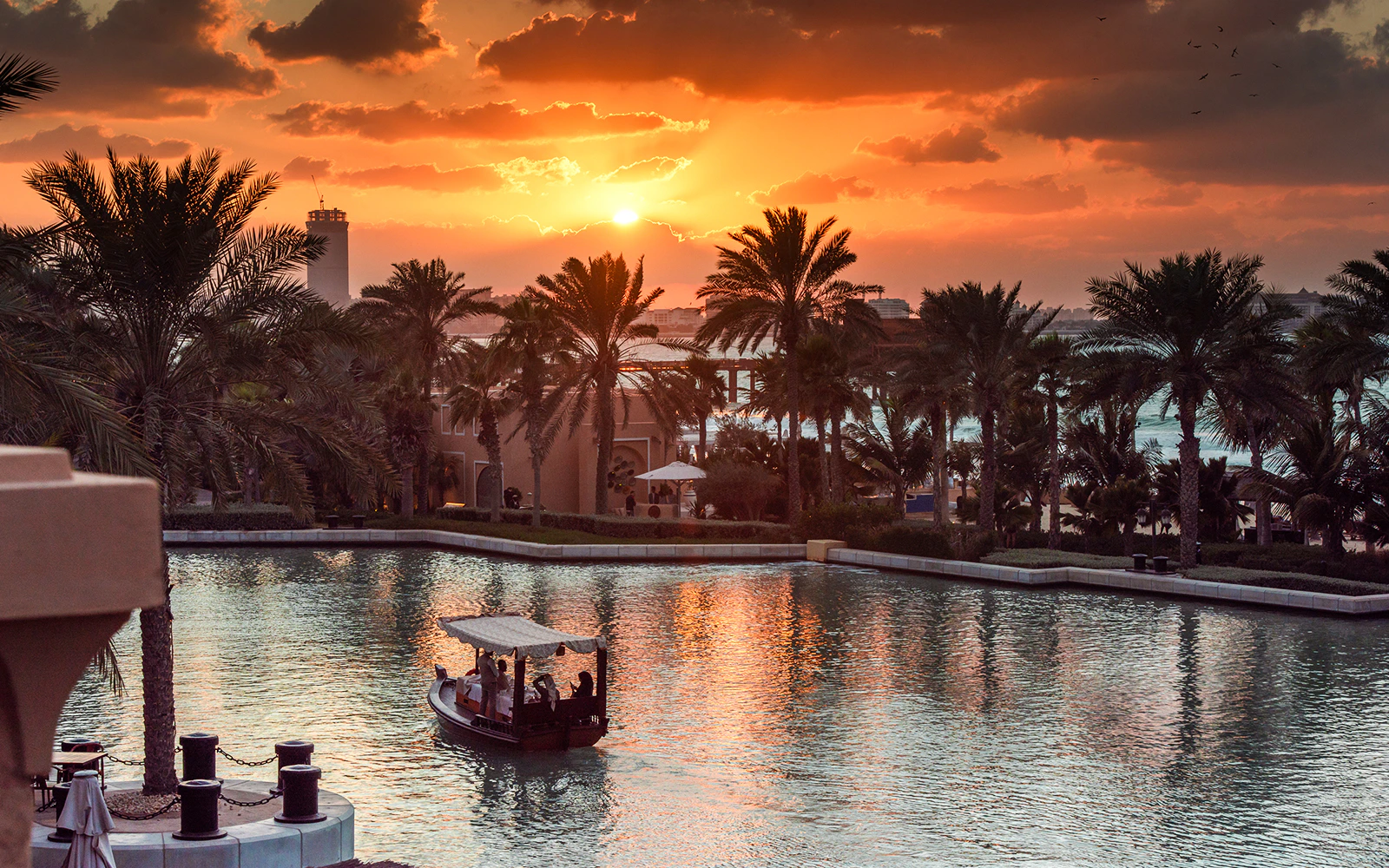 Abra boat on Dubai Water Canal at sunset with palm trees and skyline.