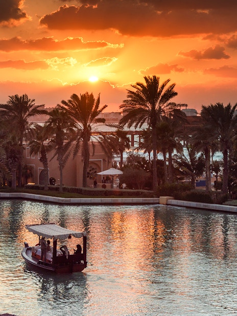 Abra boat on Dubai Water Canal at sunset with palm trees and skyline.