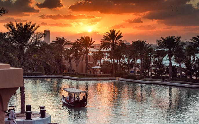 Abra boat on Dubai Water Canal at sunset with palm trees and skyline.