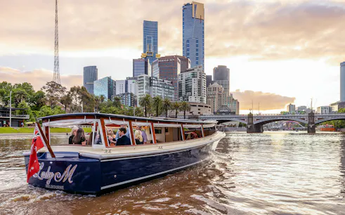 Cruise boat on Yarra River with Melbourne skyline at sunset.