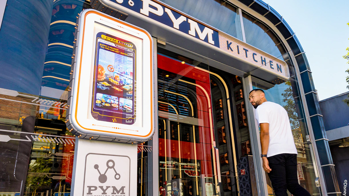Entrance of PYM Kitchen at Disneyland Paris with a digital menu display.