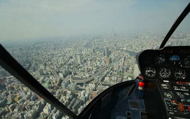 Helicopter cockpit view over Tokyo cityscape with Tokyo Skytree in the distance.