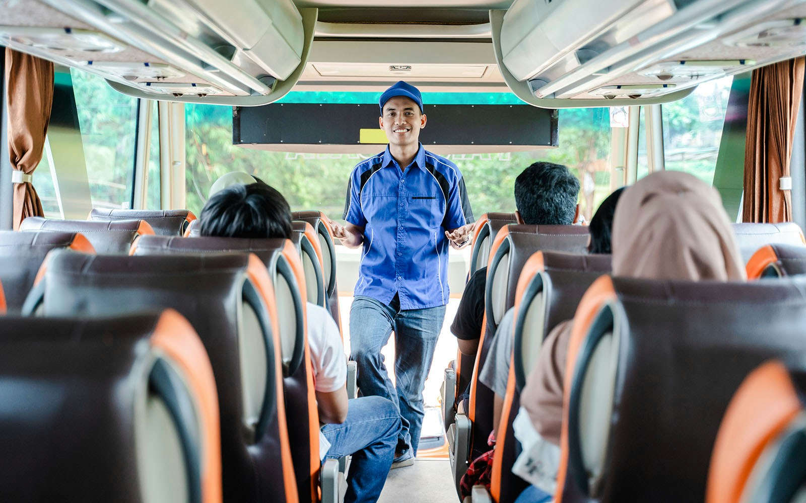 Bus crew member in uniform briefs passengers before departure.