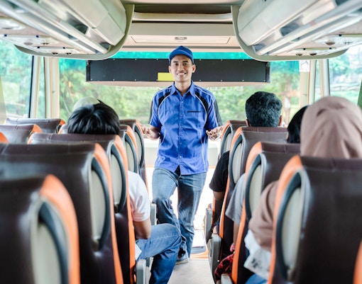 Bus crew member in uniform briefs passengers before departure.