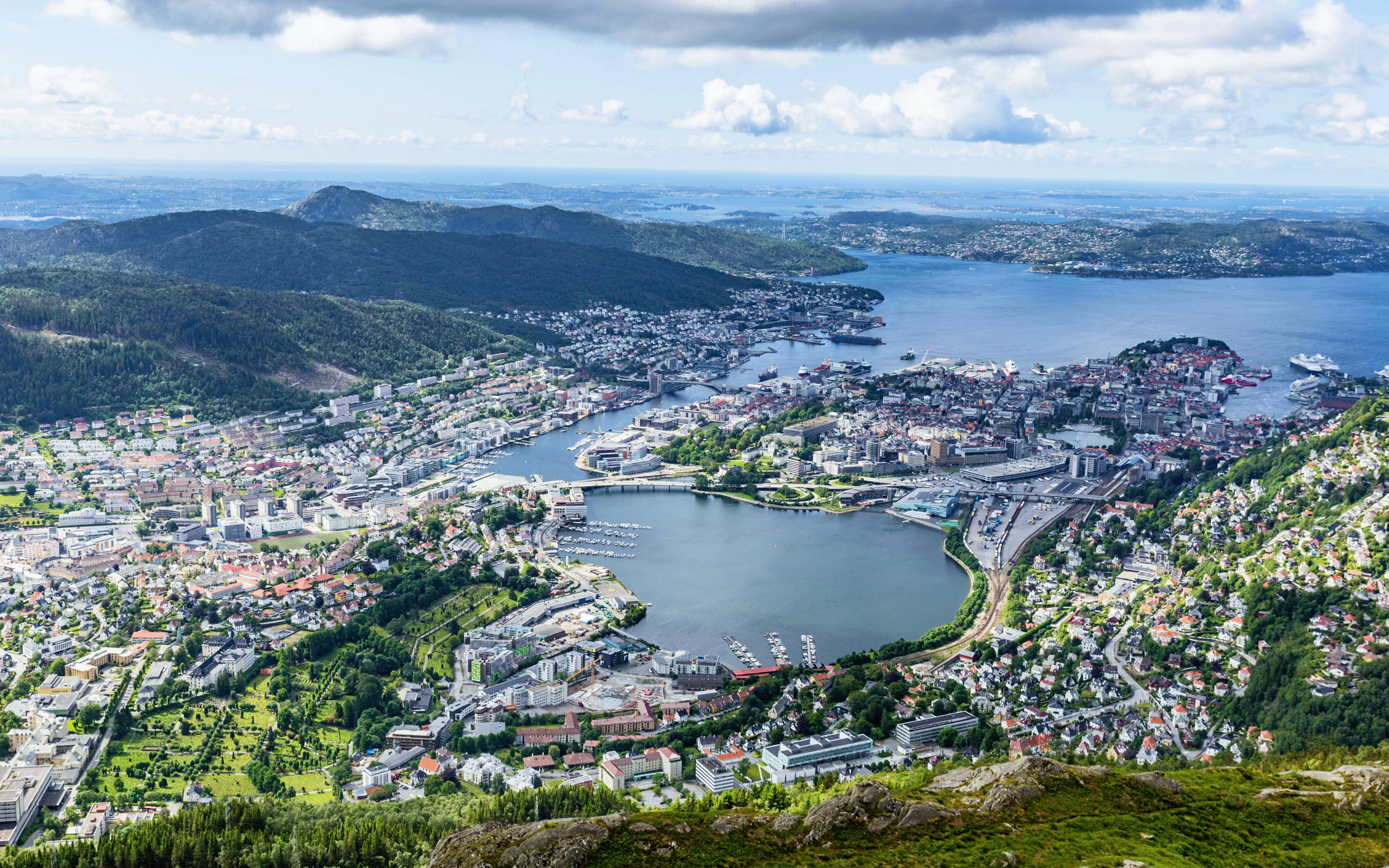 Bergen cityscape and harbor view from Mount Ulriken, Norway, with surrounding mountains and sea.
