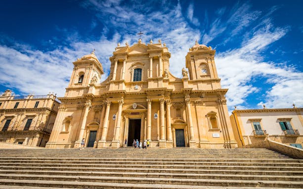 Baroque cathedral facade in Noto, Sicily, with steps leading to entrance.