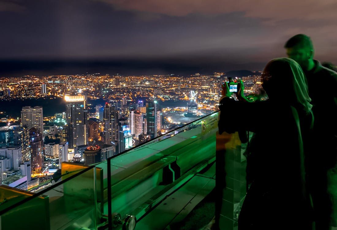 People enjoying night view from KL Tower Skydeck, city lights in background.