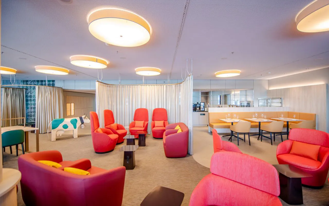 Seating area in Marhaba Lounge at Zurich Airport with red chairs and dining tables.
