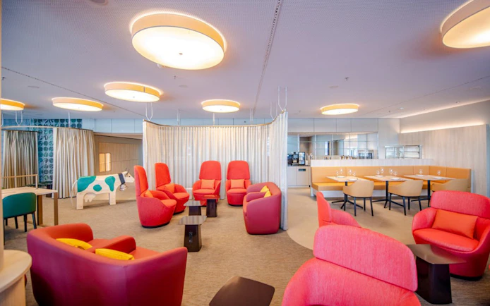 Seating area in Marhaba Lounge at Zurich Airport with red chairs and dining tables.
