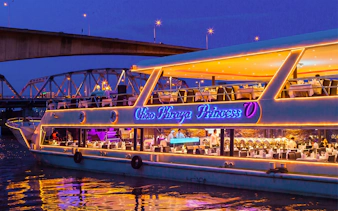 Chao Phraya Princess cruise lit up at night under a bridge, tables set for New Year's Eve dinner.
