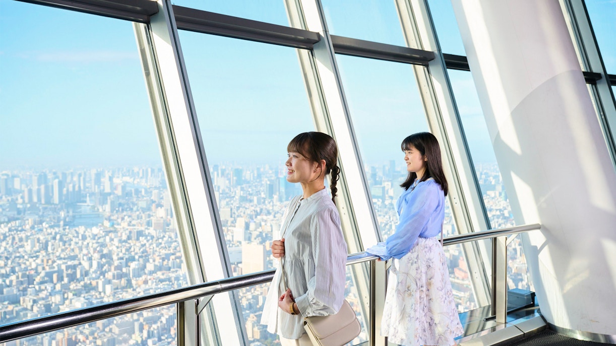 Tourists on Tembo Deck overlooking Tokyo skyline with soft drink and snack.
