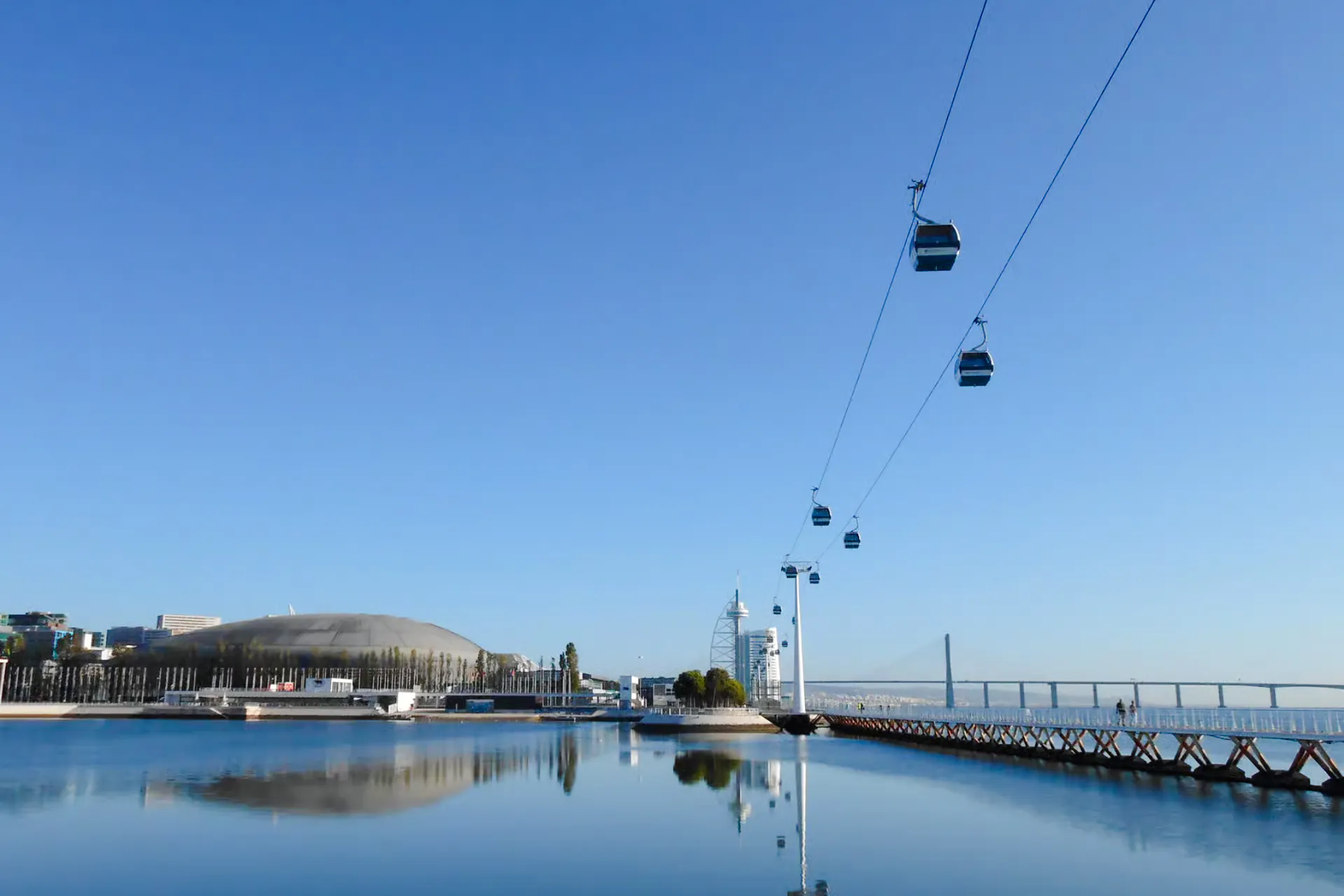 Lisbon cable cars over Tagus River with cityscape and Vasco da Gama Bridge in view.