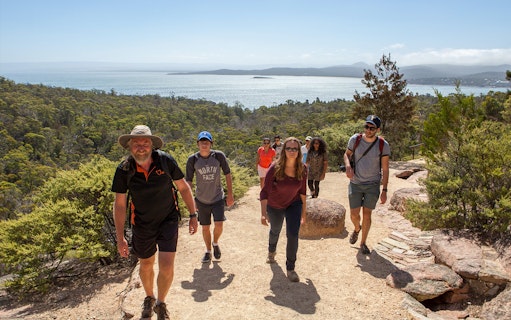 Group hiking on a trail with views of Wineglass Bay, Tasmania in the background.