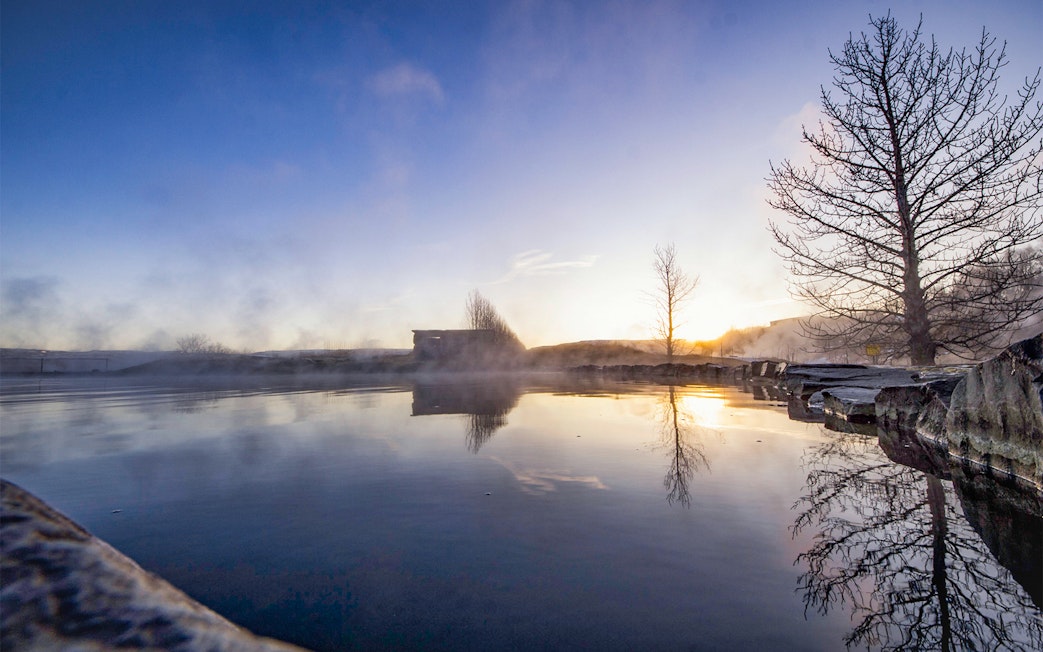 Secret Lagoon hot spring at sunrise, Gamla Laugin, Iceland, with steam rising from the water.