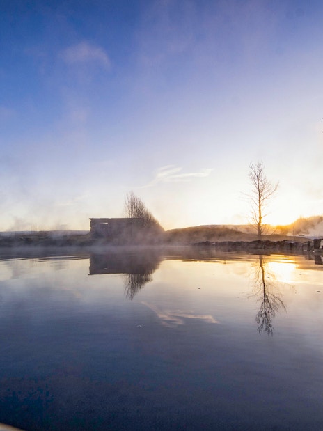 Secret Lagoon hot spring at sunrise, Gamla Laugin, Iceland, with steam rising from the water.