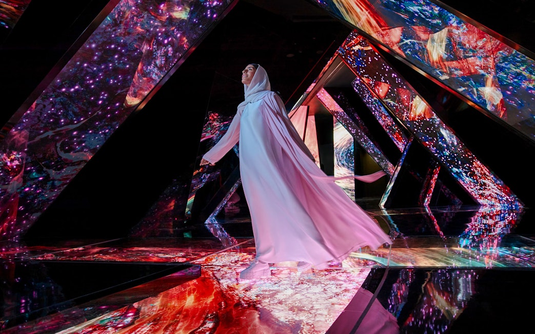 Person walking through a vibrant, mirrored installation at AYA Universe.