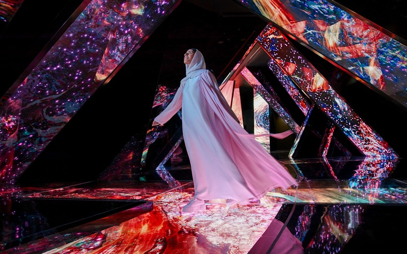 Person walking through a vibrant, mirrored installation at AYA Universe.