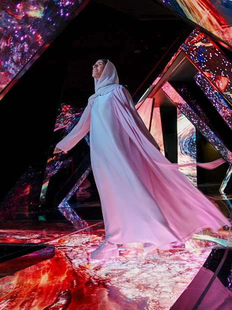 Person walking through a vibrant, mirrored installation at AYA Universe.