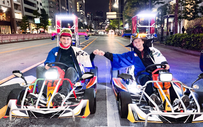 Two people in costumes fist-bumping while go-karting at night in Shibuya, Tokyo.
