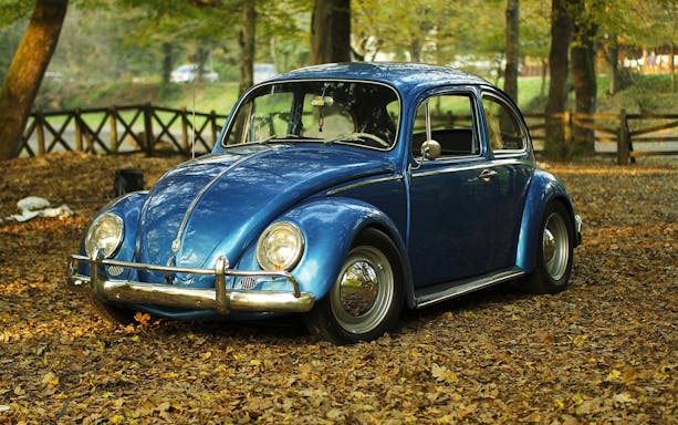 Vintage blue car parked on a leaf-covered path, part of Etna wine-tasting tour.