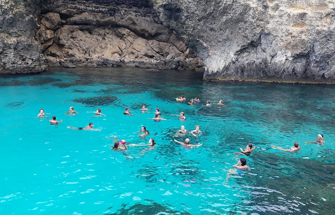 People swimming in the clear waters of Blue Lagoon, Malta, surrounded by rocky cliffs.
