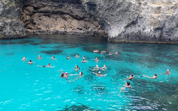 People swimming in the clear waters of Blue Lagoon, Malta, surrounded by rocky cliffs.