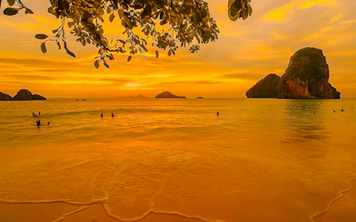 Sunset view of Krabi's islands with swimmers and a longtail boat in the distance.