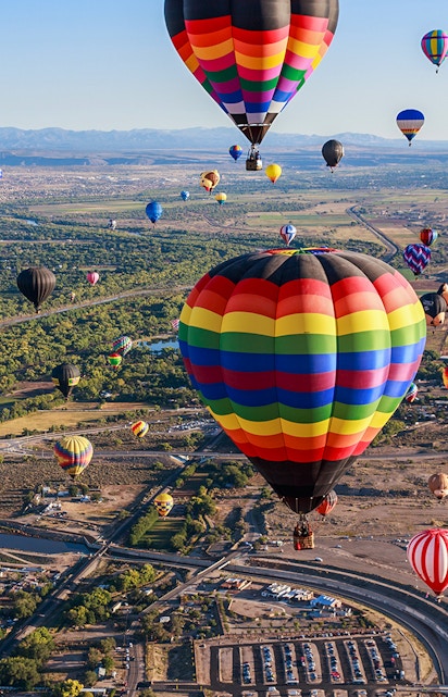 Hot air balloons floating over Albuquerque landscape during annual festival.