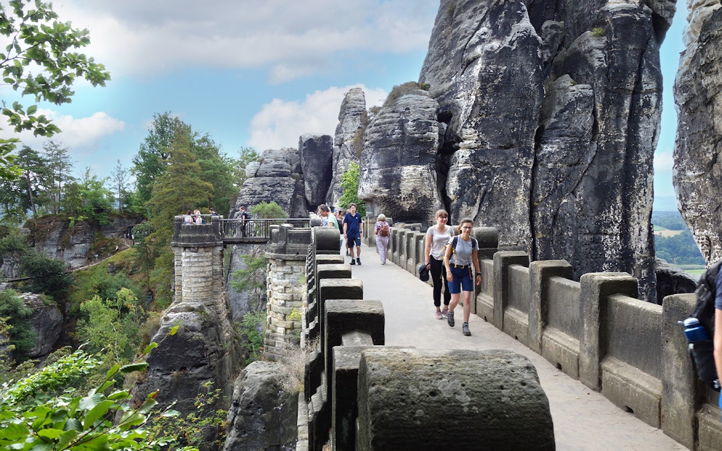 Visitors walking on Bastei Bridge with rock formations in Saxon Switzerland, Germany.