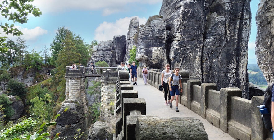 Visitors walking on Bastei Bridge with rock formations in Saxon Switzerland, Germany.