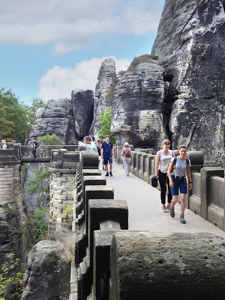 Visitors walking on Bastei Bridge with rock formations in Saxon Switzerland, Germany.