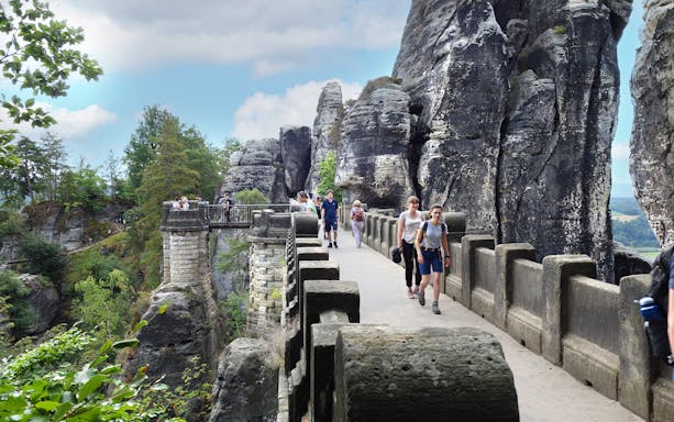 Visitors walking on Bastei Bridge with rock formations in Saxon Switzerland, Germany.