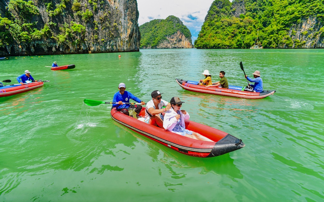 Tourists kayaking in Phang Nga Bay with limestone cliffs in the background.
