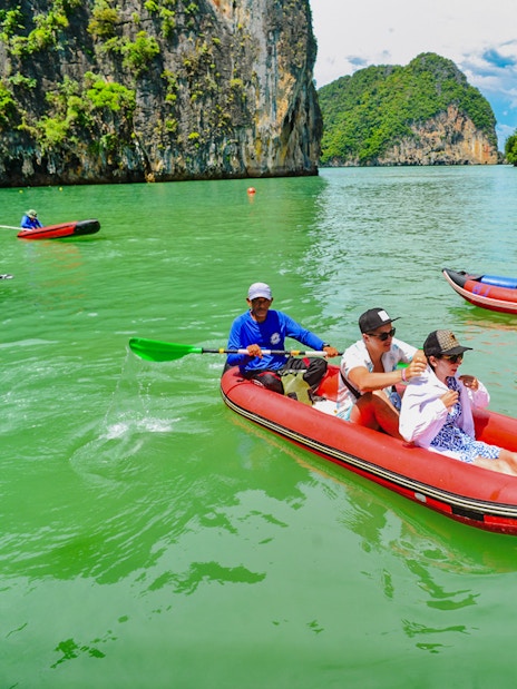 Tourists kayaking in Phang Nga Bay with limestone cliffs in the background.