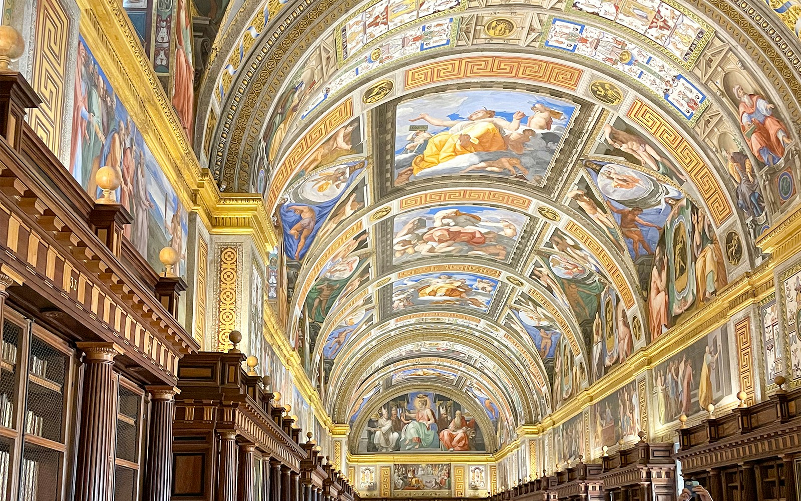 El Escorial Library ceiling with detailed frescoes and ornate wooden bookshelves.
