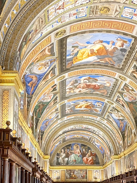 El Escorial Library ceiling with detailed frescoes and ornate wooden bookshelves.