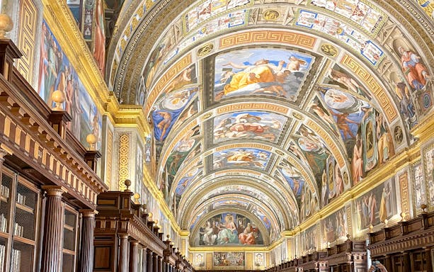 El Escorial Library ceiling with detailed frescoes and ornate wooden bookshelves.