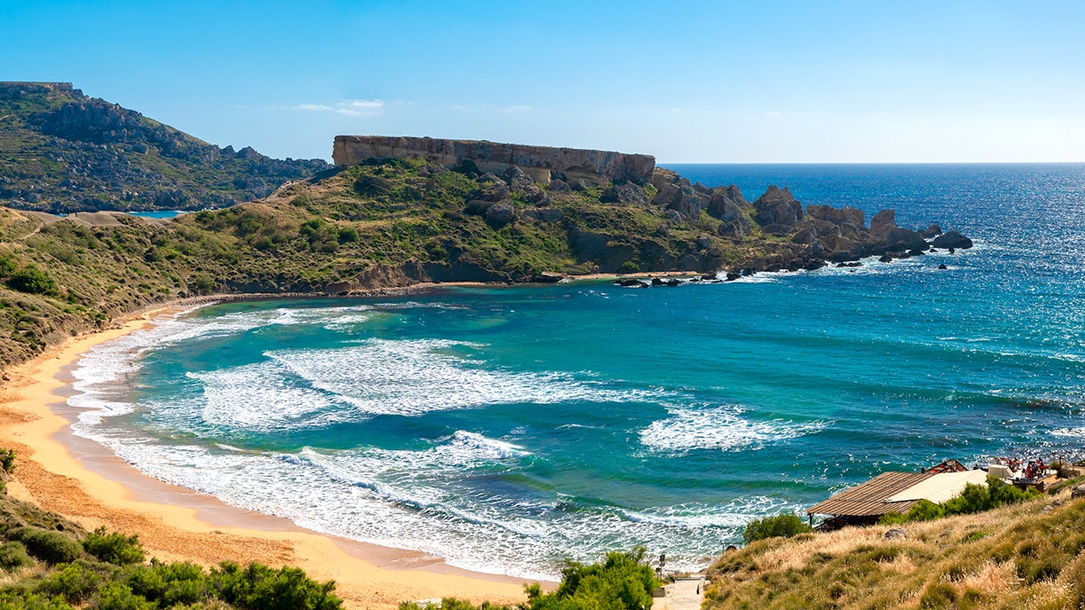 Golden Bay beach with clear waters and sunbathers, Malta.