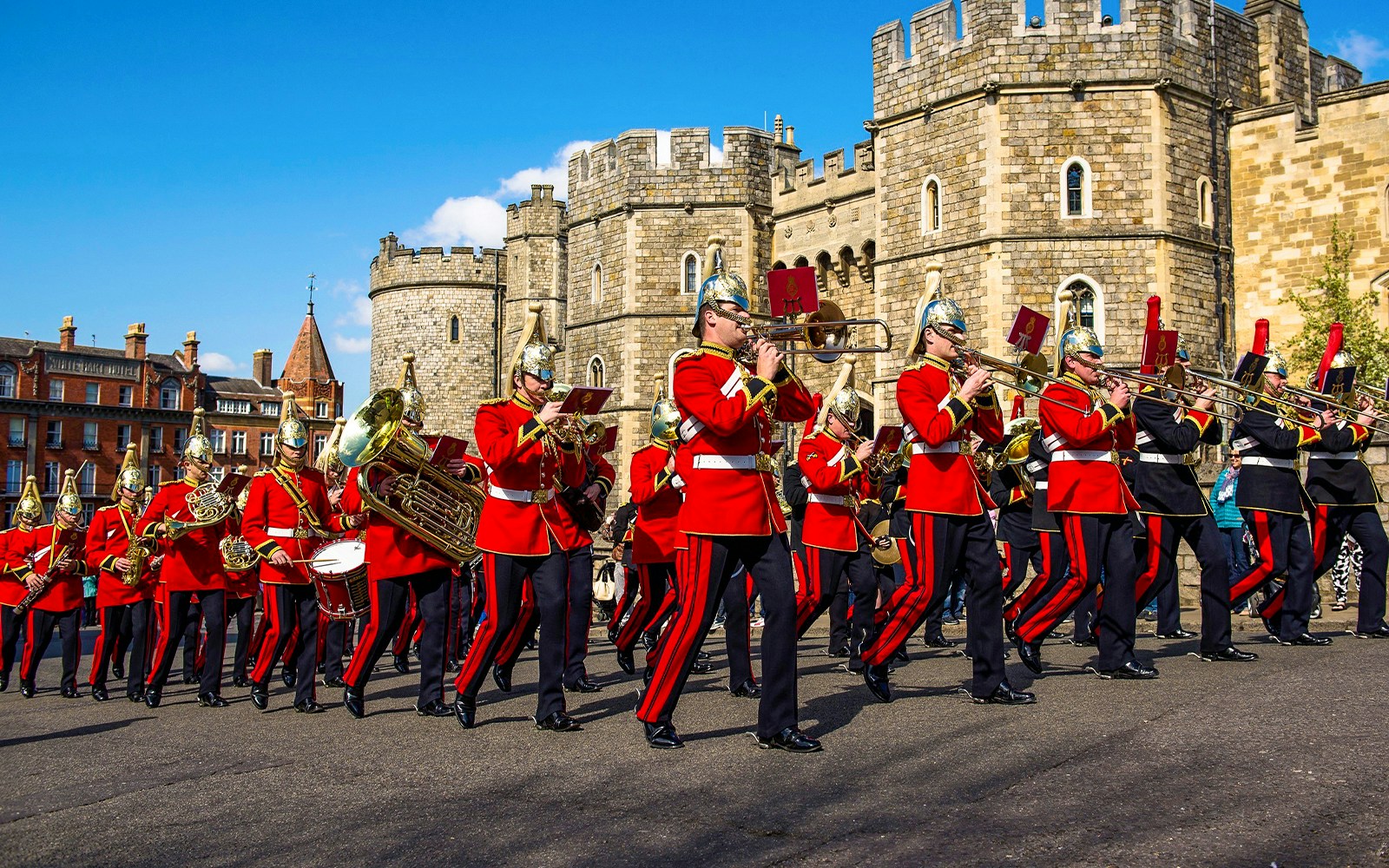 Guards in red uniforms marching with instruments in front of Windsor Castle.