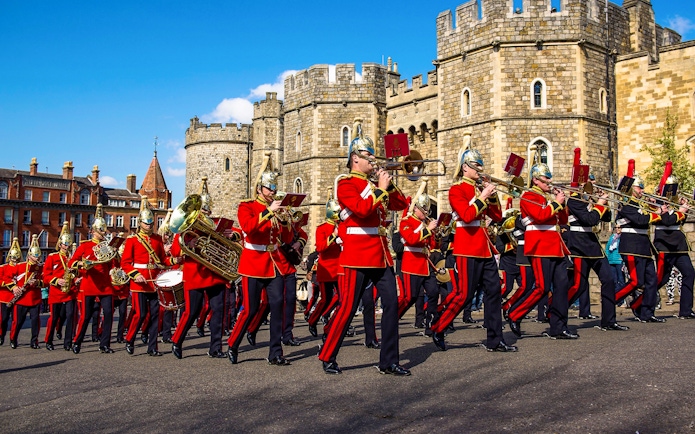 Guards in red uniforms marching with instruments in front of Windsor Castle.