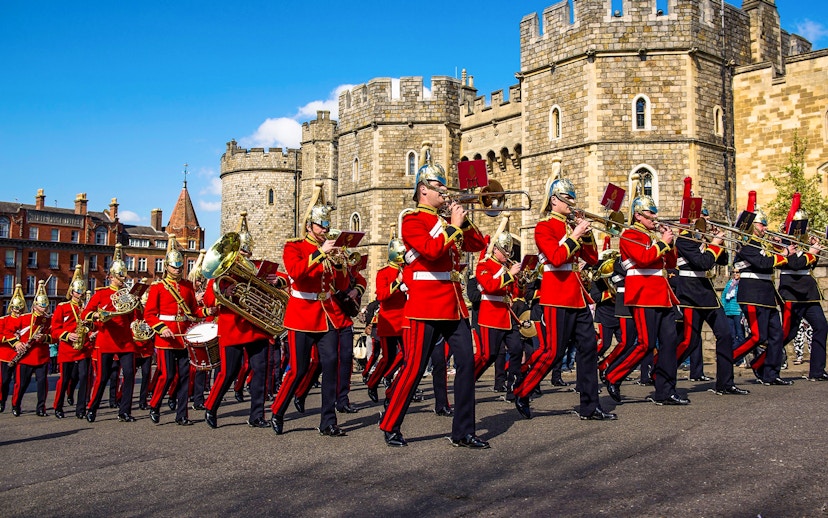 Guards in red uniforms marching with instruments in front of Windsor Castle.