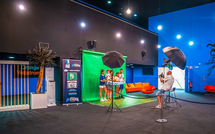Visitors posing for a photo at the OM Stadium Tour with a green screen backdrop.