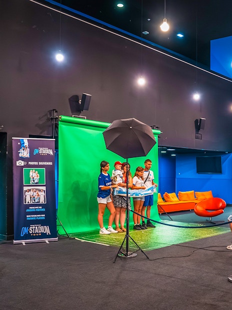 Visitors posing for a photo at the OM Stadium Tour with a green screen backdrop.